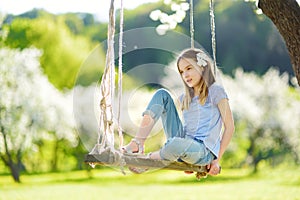 Cute little girl having fun on a swing in blossoming old apple tree garden outdoors on sunny spring day