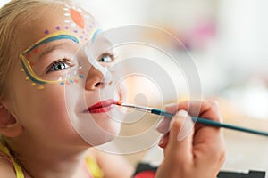 Cute little girl having her face painted for Halloween party. Halloween or carnival family lifestyle background. Face painting.