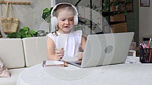 Cute little girl in headphone sitting at the table with laptop.