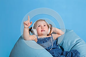 Cute little girl in headphones listening to music using a tablet and smiling while sitting on blue big bag