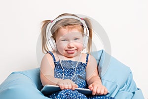 Cute little girl in headphones listening to music using a tablet and smiling while sitting on blue big bag