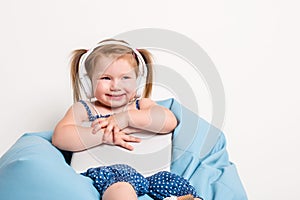 Cute little girl in headphones listening to music using a tablet and smiling while sitting on blue big bag