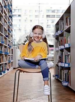 Cute little girl with headphones reading book on chair