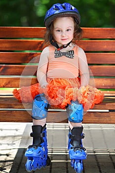 Cute little girl in helmet and roller skates sits