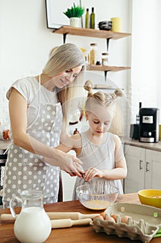 Cute little girl helps mom bake cookies in the kitchen