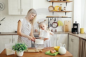 Cute little girl helps mom bake cookies in the kitchen