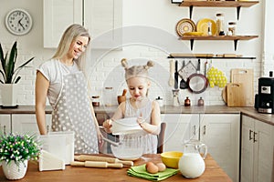 Cute little girl helps mom bake cookies in the kitchen