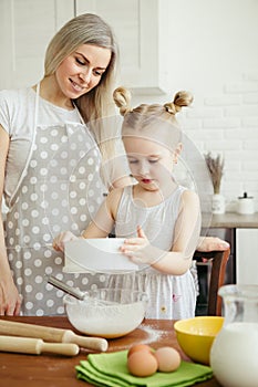 Cute little girl helps mom bake cookies in the kitchen