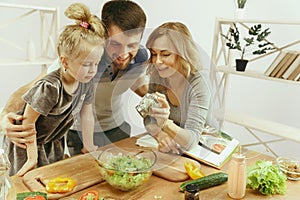 Cute little girl and her beautiful parents are cutting vegetables in kitchen at home