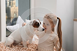 Cute little girl with her dog near window at home. Childhood pet