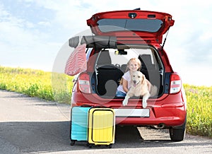 Cute little girl and her dog in open car trunk . Space for text