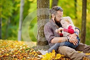 Cute little girl and her father having fun on beautiful autumn day. Happy child playing in autumn park. Kid gathering yellow fall