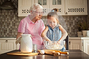 Cute little girl and her grandmother cooking on kitchen.