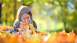Cute little girl with her hair lies on fallen foliage in a beautiful park