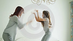 Cute little girl with her loving mother have fun dancing modern style together jumping and giving high five on bed