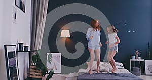 Cute little girl with her loving mother have fun dancing modern style together jumping and giving high five on bed