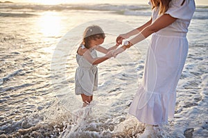 Cute little girl and her mixed race mother playing in the water at the beach. Young daughter and her mom spending