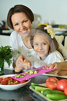 Cute little girl with her mother cooking together at kitchen table