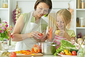 Cute little girl with her mother cooking together at kitchen table