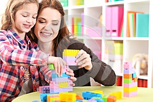 Cute little girl and her mother playing colorful plastic blocks