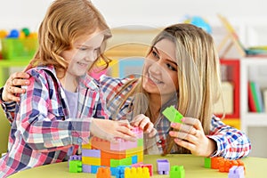 Cute little girl and her mother playing colorful plastic blocks