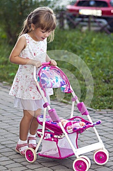 Cute little girl with her toy carriage and doll outdoors