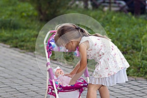 Cute little girl with her toy carriage and doll outdoors