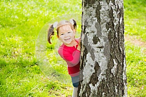 Cute little girl hiding behind huge tree