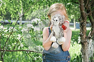 Cute little girl hiding behind toy cat. blonde girl hides her face