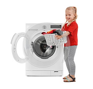 Cute little girl holding basket with laundry near washing machine