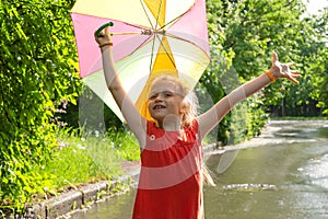 Cute little girl holding a colorful umbrella in her hands and enjoying the sun after the rain
