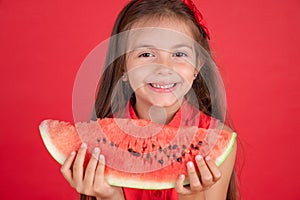 Cute little girl holding, eating  juicy slice of watermelon over red background