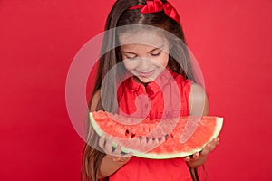 Cute little girl holding, eating  juicy slice of watermelon over red background