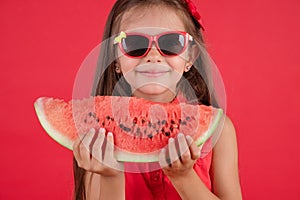 Cute little girl holding, eating  juicy slice of watermelon over red background