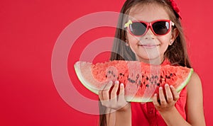 Cute little girl holding, eating  juicy slice of watermelon over red background