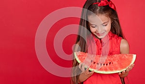 Cute little girl holding, eating  juicy slice of watermelon over red background