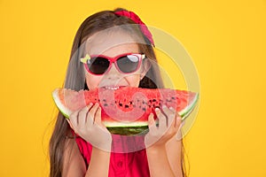 Cute little girl holding, eating  juicy slice of watermelon over yellow background