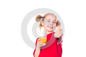 Cute little girl holding glass with juice with thumb up