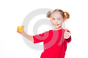 Cute little girl holding glass with juice with thumb up