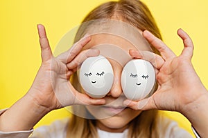 Cute little girl holding hands easter eggs with cute face and sleepy eyes on yellow background. Happy Easter concept