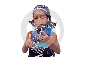 Cute little girl holding mobile phone and showing her thumb up s