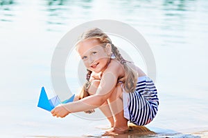 Cute little girl holding origami boat outdoors