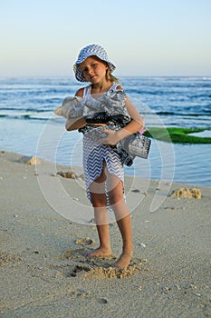 Cute little girl holding small white chihuahua dog with pink tail on the beach. Take care of the pet. Dog covered with scarf.