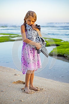Cute little girl holding small white chihuahua dog with pink tail on the beach. Take care of the pet. Dog covered with scarf.