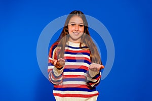 Cute little girl holding something with her palms, offering it to the camera. Isolated on blue studio background