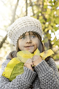 Cute little girl holding yellow maple leaves in her hands while walking in the autumn sunny park - Portrait of little girl