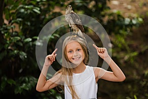 A cute little girl holds an eagle on her shoulder. Children and nature. Summer day in the park