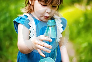 Cute little girl holds an empty plastic bottle in the fresh air, in nature, in the forest. Used plastic bottle in hand. Concern fo