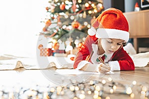 Cute little girl by the holiday tree, putting her hopes and dreams into a letter for Santa Claus