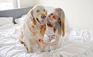 Cute Little Girl Hugging With Beautiful Golden Retriever Dog On Bed In The Morning